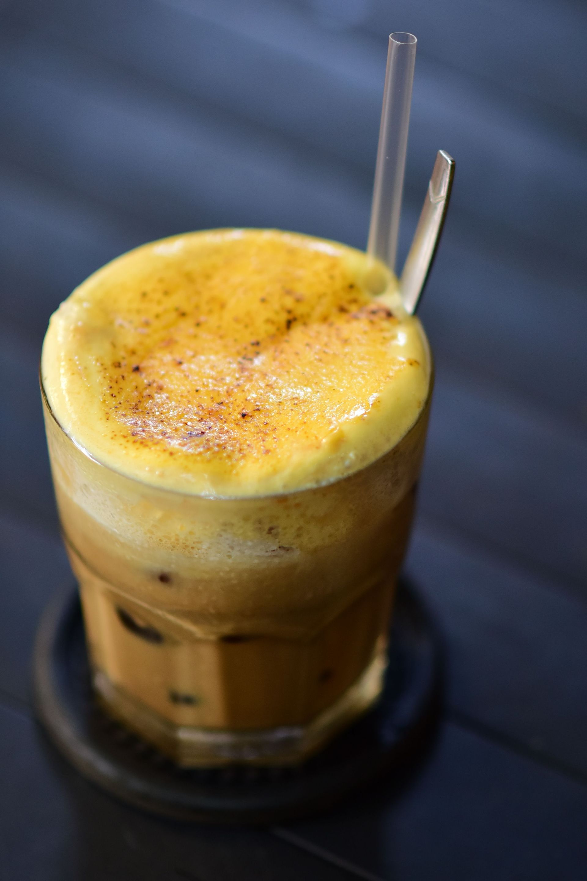 Chilled coffee served in a glass with a frothy yellow egg topping and straws.